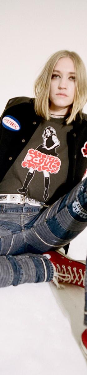 A woman wearing a black X-Girl patch varsity jacket and graphic tee with patchwork denim jeans