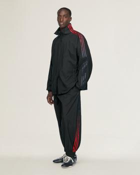A man in a black Y-3 nylon track top and track pants with red three stripes and navy sneakers