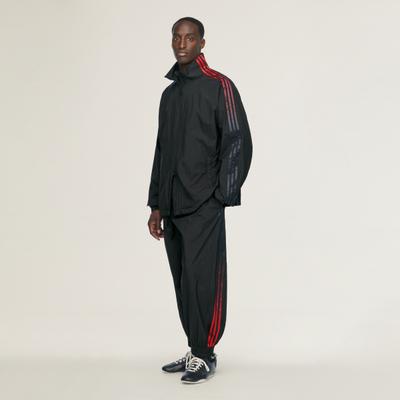 A man in a black Y-3 nylon track top and track pants with red three stripes and navy sneakers