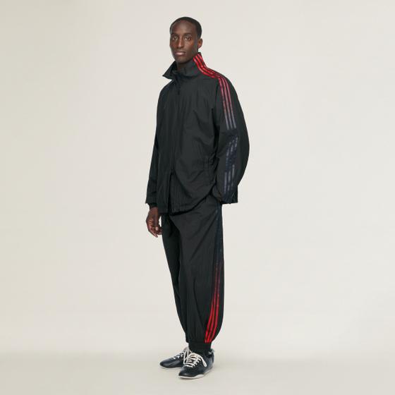A man in a black Y-3 nylon track top and track pants with red three stripes and navy sneakers