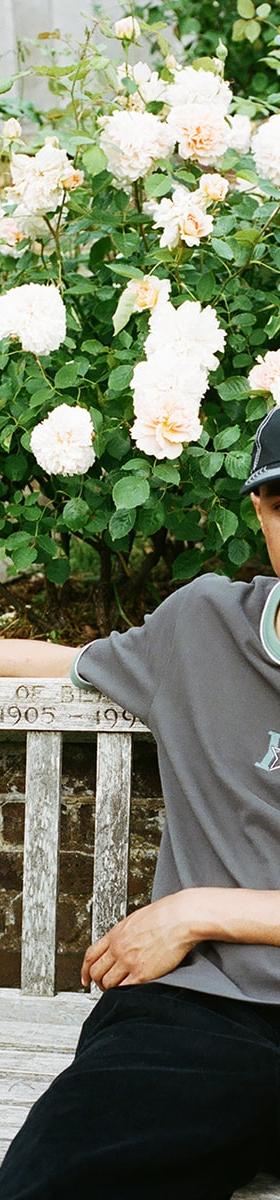 A man wearing a grey Yardsale ringer T-shirt and black cap sitting on a park bench