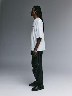 A man wearing a white oversized YEMAT t-shirt with black wide-leg trousers
