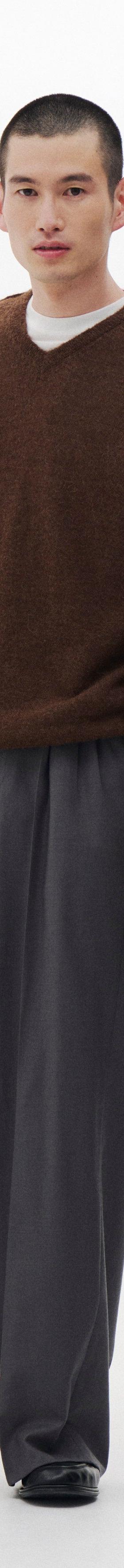 A man wearing a brown mohair V-neck sweater and grey wide-leg pleated trousers
