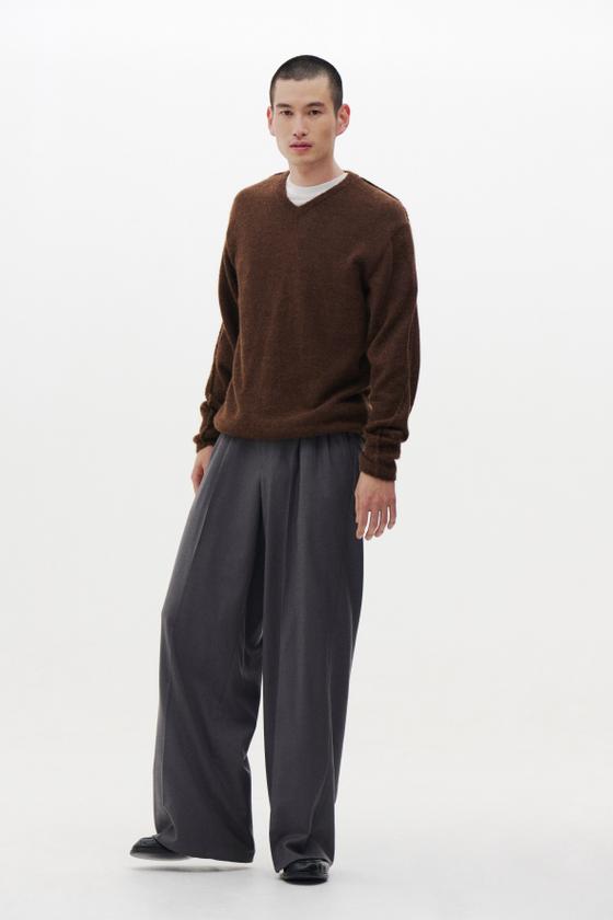A man wearing a brown mohair V-neck sweater and grey wide-leg pleated trousers