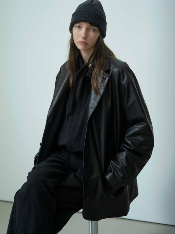 A model wearing an oversized black YOKO SAKAMOTO coat with wide trousers and a knit beanie