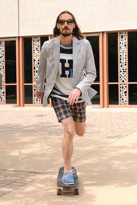 A man wearing blue Yuketen boat shoes with plaid shorts and a checked blazer, riding a skateboard