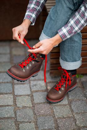 A man lacing up brown leather Zamberlan hiking boots with red laces