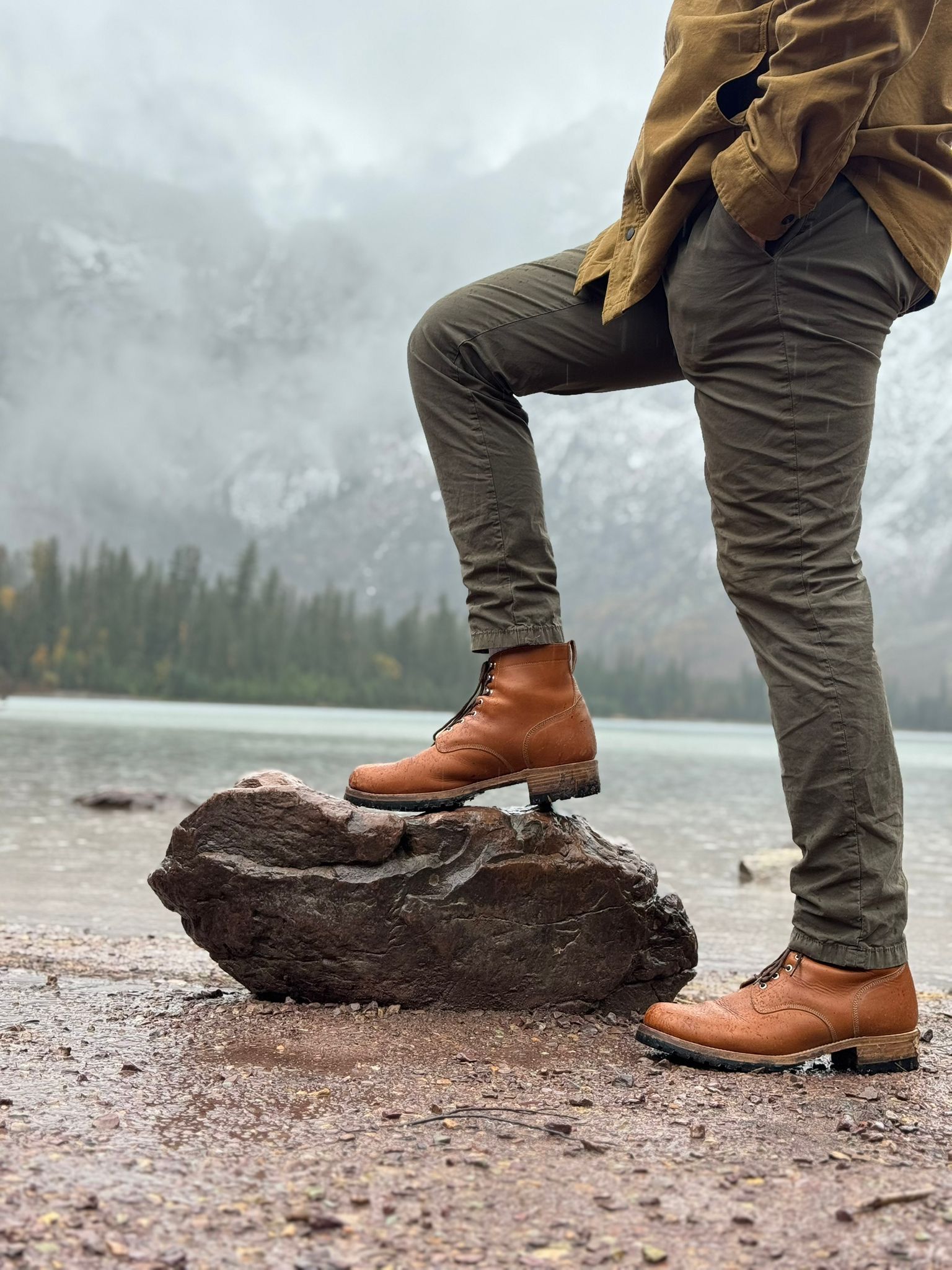 A Saddleback Huntsman boot in Natural on a rock beside a lake