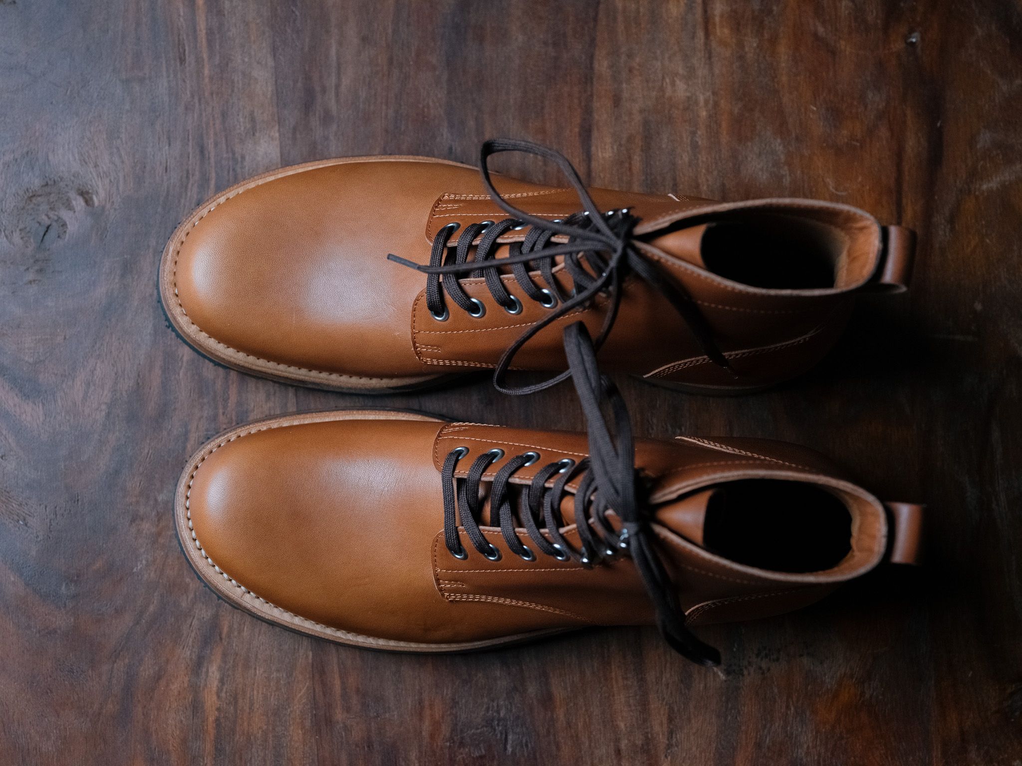A pair of Saddleback Huntsman boots in Natural leather from above, on dark wood