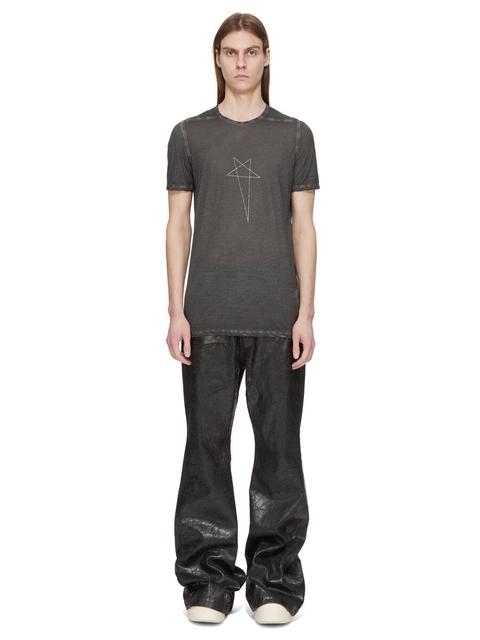 A man wearing a long washed-charcoal T-shirt with a thin pentagram print, over black waxed flared jeans stacked over off-white sneakers, against a plain white background.