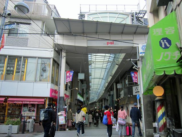 A man wearing a dark jacket and backpack walking into the covered Pal Shopping Street arcade in Koenji, shopfronts and signs lining the pavement