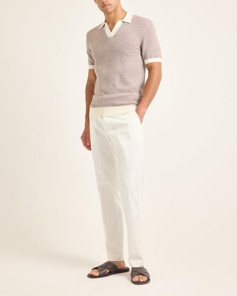 A man wearing a taupe-and-white textured knit open-collar polo with cream trim, off-white tailored cotton trousers and dark brown leather cross-strap sandals without socks, standing on a plain cream background.