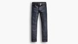 A pair of dark rigid raw indigo button-fly jeans with copper rivets, laid flat in front view on a pale grey background.